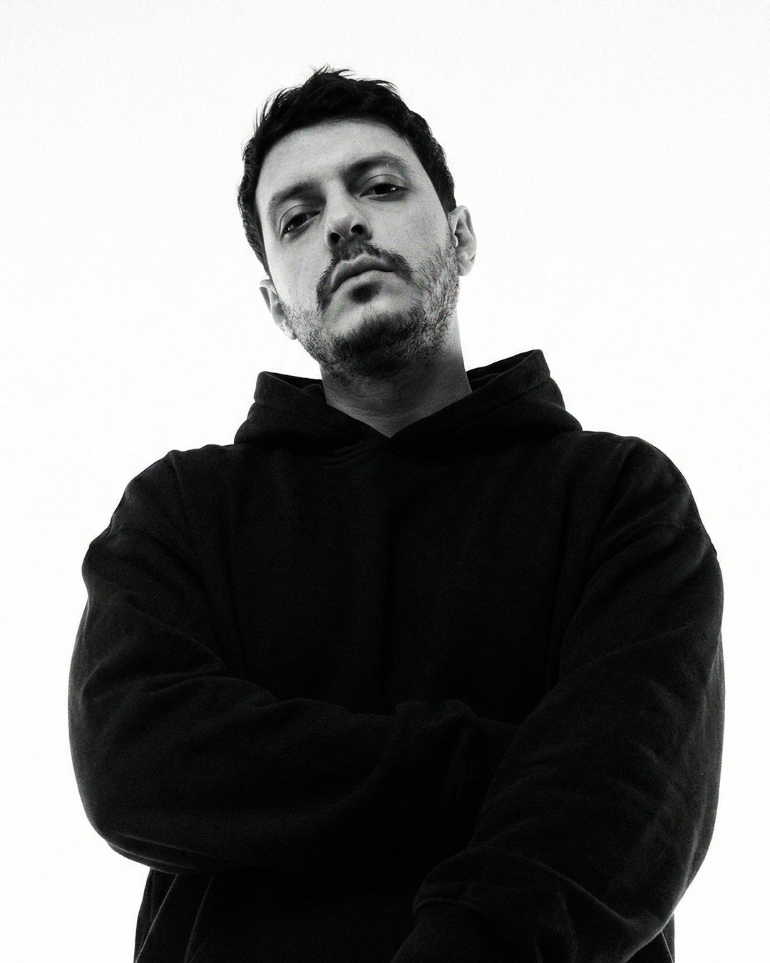 offrami, black and white press portrait: black hoodie, arms crossed, white background